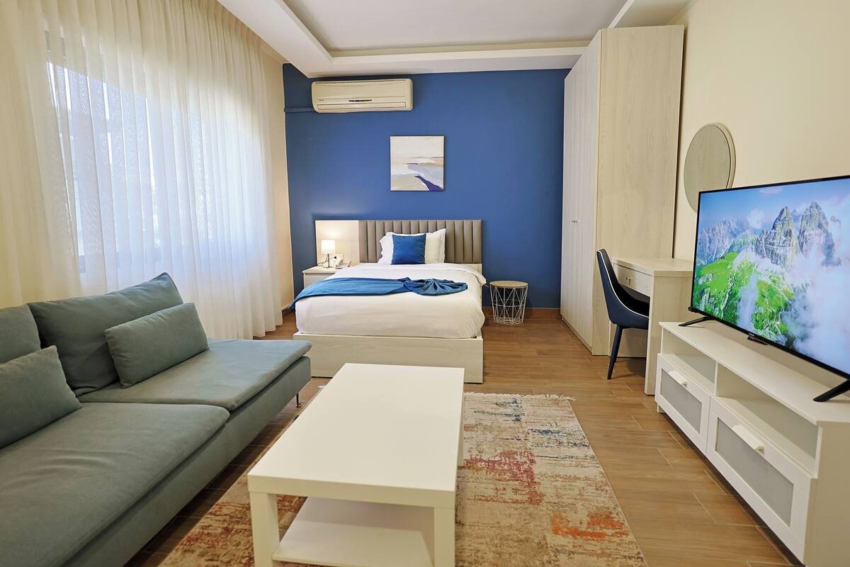 A modern hotel room with a bed, a sofa, a TV, and a desk.