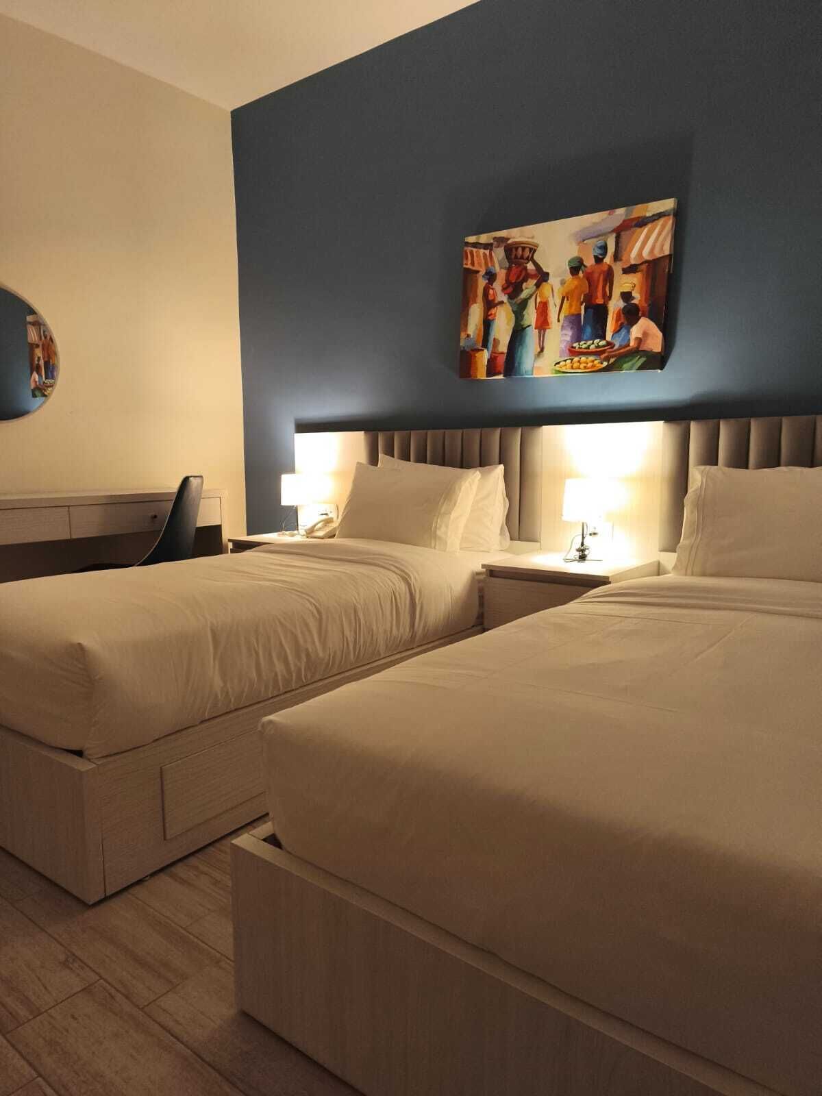 A hotel room with two beds, a blue accent wall, and a painting above the beds.