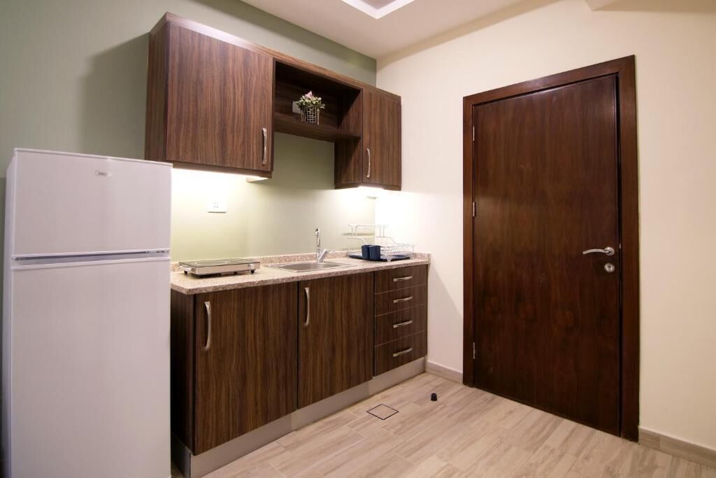 Une cuisine de taille réduite, avec des meubles de rangement en bois, un réfrigérateur blanc et une porte en bois.