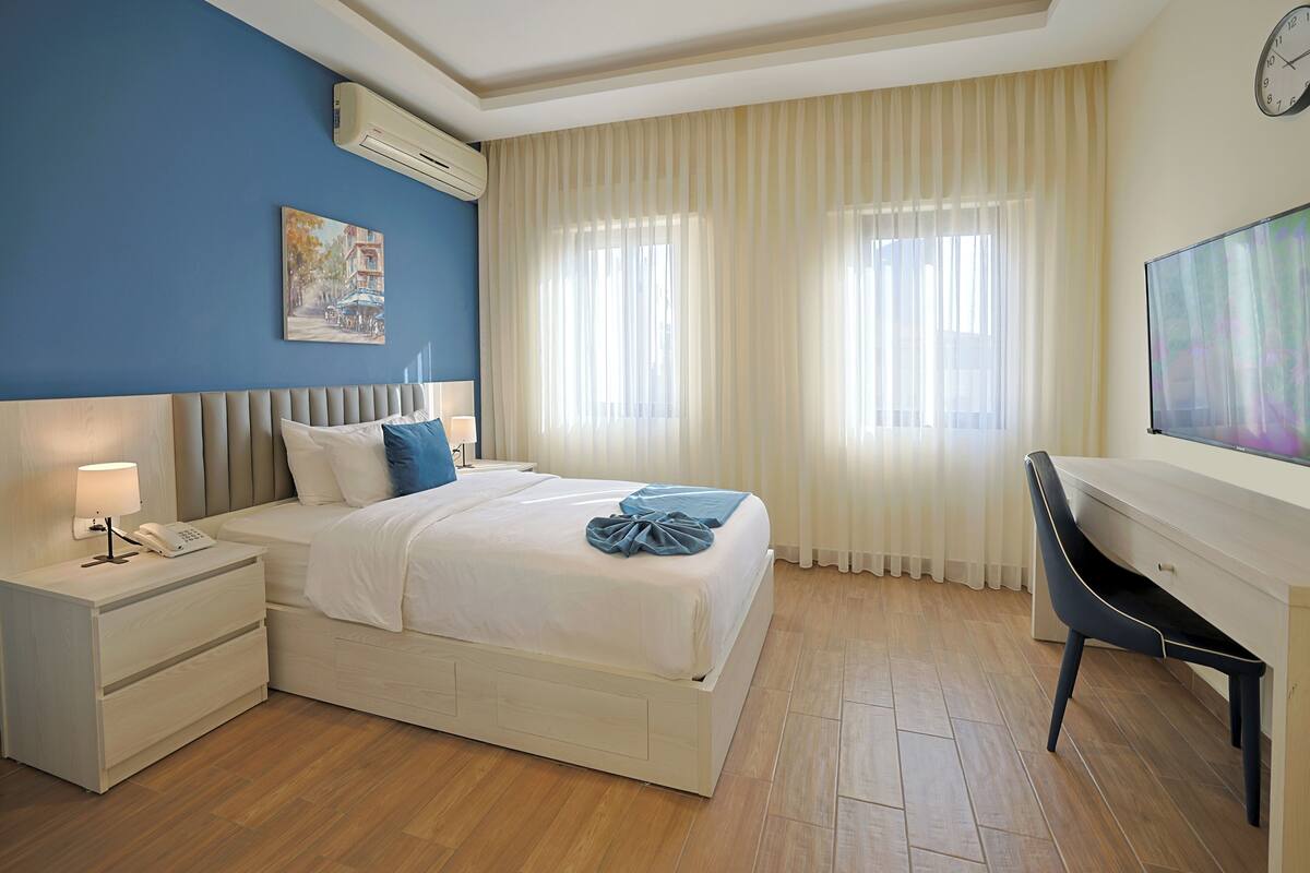 A hotel room with a bed, bedside table with a lamp, a desk, and a chair.