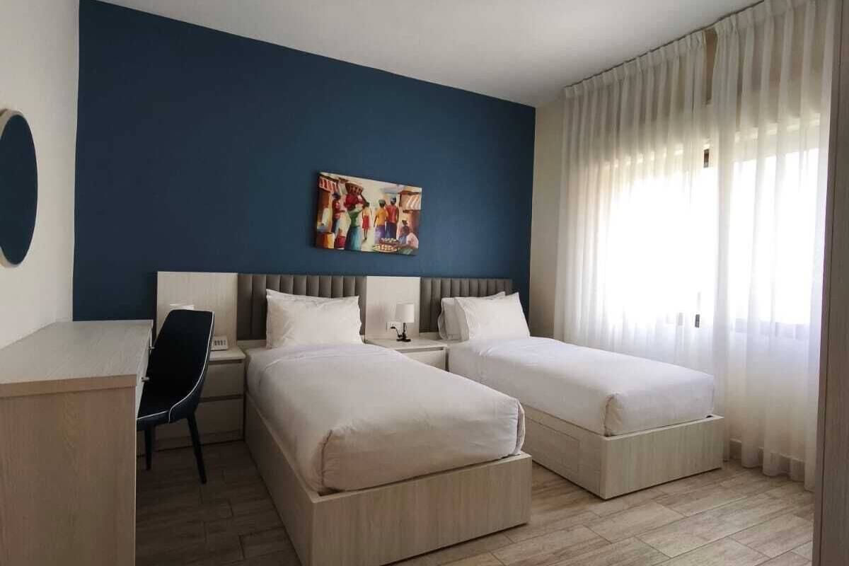 A hotel room with two beds, a desk, a chair, and a painting on the wall.