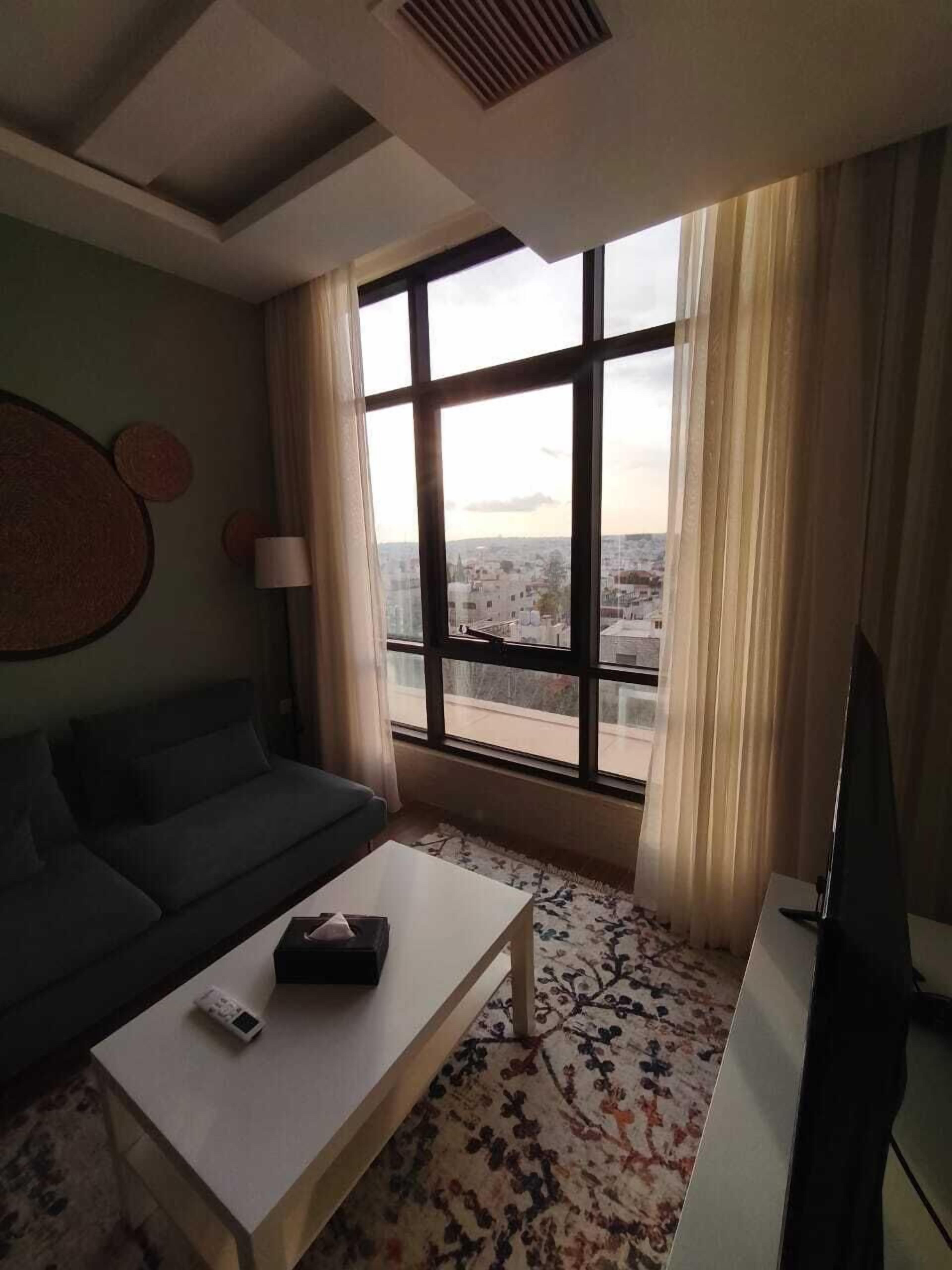 A modern living room with a sofa, a coffee table, a TV, and a large window with curtains.