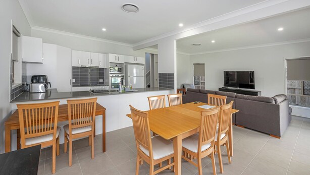 Una cocina moderna con armarios blancos, un comedor con sillas de madera y un sofá gris en la sala.