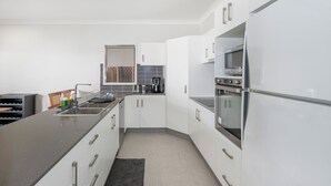 Una cocina moderna con armarios blancos, encimera de acero inoxidable, horno empotrado y cafetera.