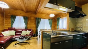 En stuga med träpanel på insidan, inredd med en soffa, ett matbord och ett köksområde.