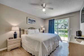 Une chambre à coucher comprenant un lit, une table de chevet, une lampe, un ventilateur de plafond et une vue sur l’extérieur.