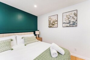 Une chambre d’hôtel avec un mur d’accent de couleur turquoise, un lit recouvert de draps blancs, deux œuvres d’art florales encadrées et un lit parfaitement fait avec des serviettes roulées.
