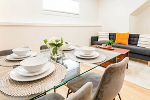 A dining area with a glass table, white plates, and a vase with flowers.