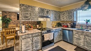 Une cuisine moderne dotée de plans de travail en granit, d’appareils électroménagers en acier inoxydable et d’un pare-feu en briques.