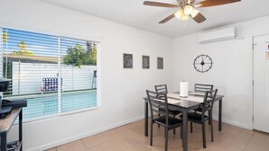 Un coin repas comprenant une table et des chaises, un ventilateur de plafond, une horloge et une fenêtre avec des stores.