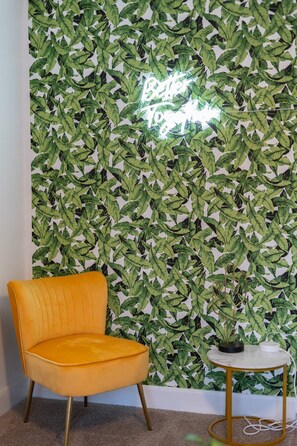 A room with a leafy wallpaper, a yellow armchair, and a small round table with a plant.