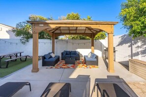 Un espace extérieur aménagé, abrité et doté d’une pergola, de deux canapés, d’une table basse et d’une table de pique-nique.