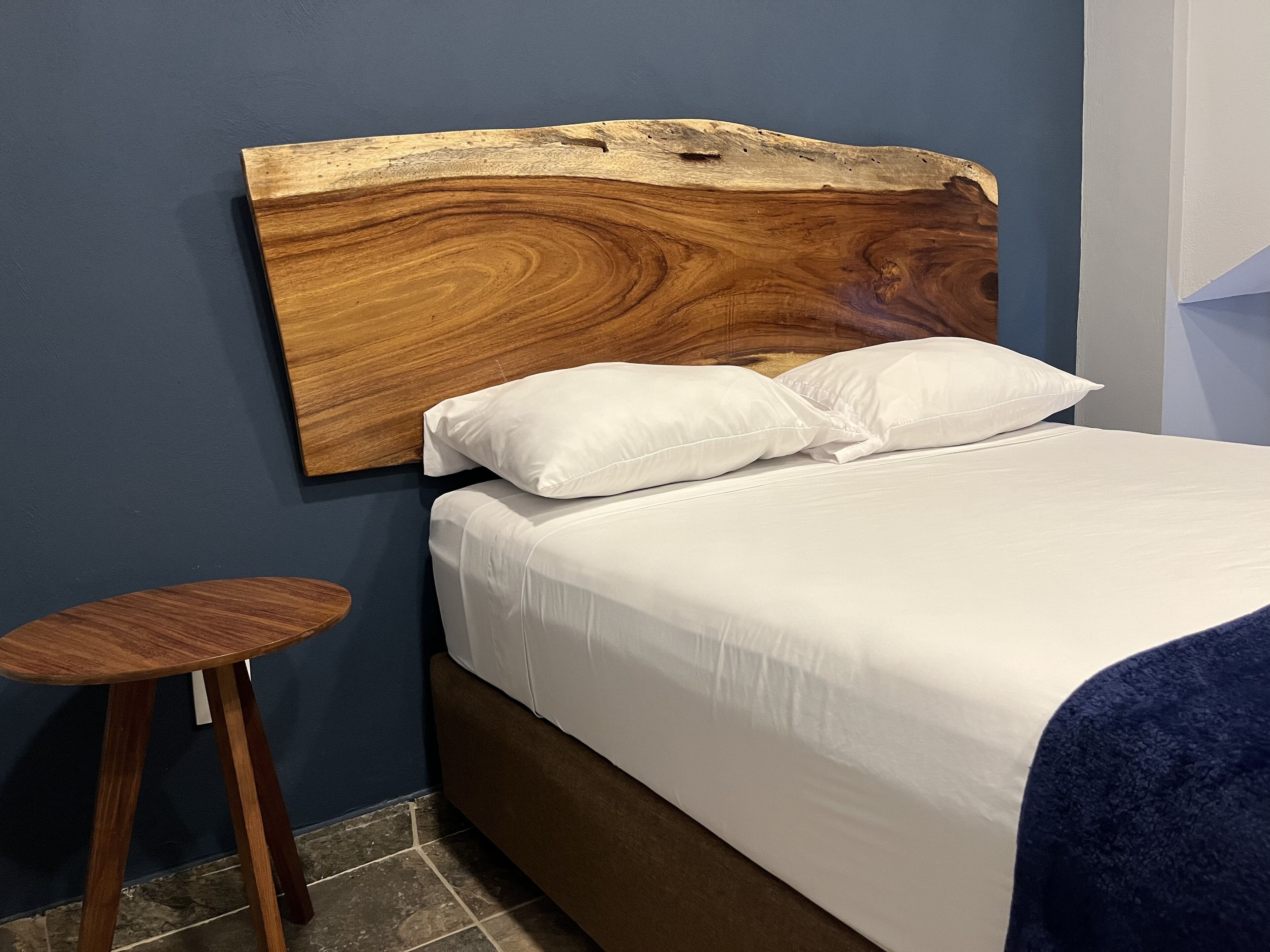 A bed with a wooden headboard, white bedding, and a small wooden stool.