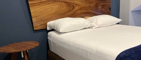 A bed with a wooden headboard, white bedding, and a small wooden stool.