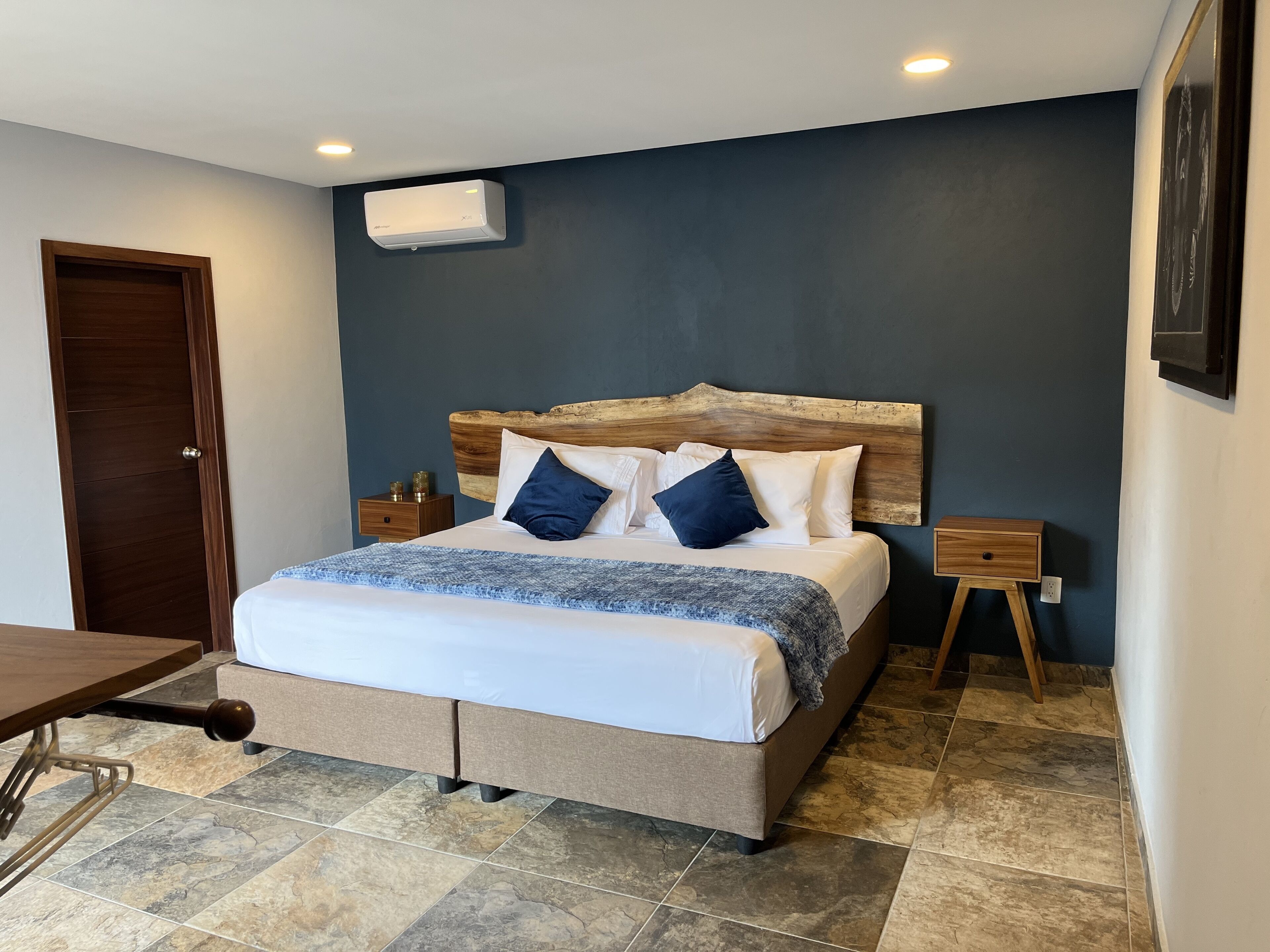 A bedroom with a bed, wooden headboard, bedside tables, and a wall-mounted air conditioner.