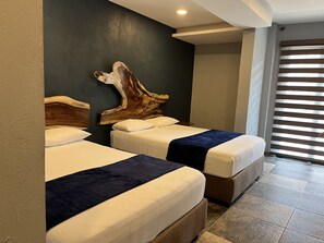 Two beds with white linens and dark blue bedspreads, a natural wood headboard, and dark gray accent wall.