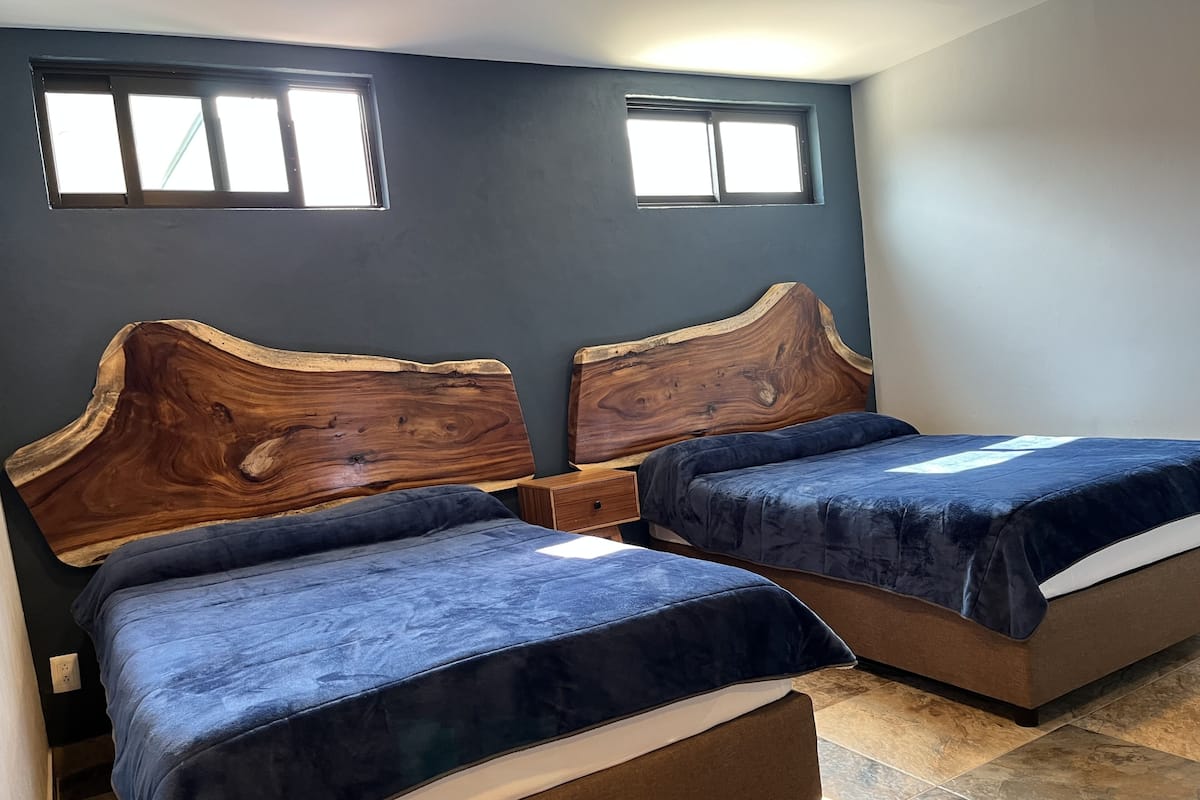 A bedroom with two beds, wooden headboards, and a dark wall.