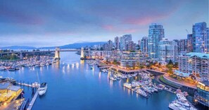 A marina with boats docked, a bridge in the background, and modern high-rise buildings.