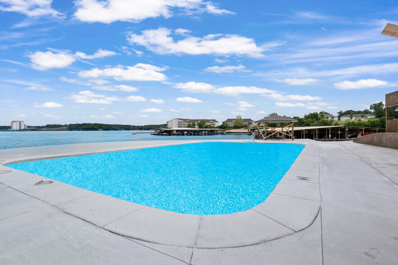 A swimming pool with a clear blue water, surrounded by a concrete deck.
