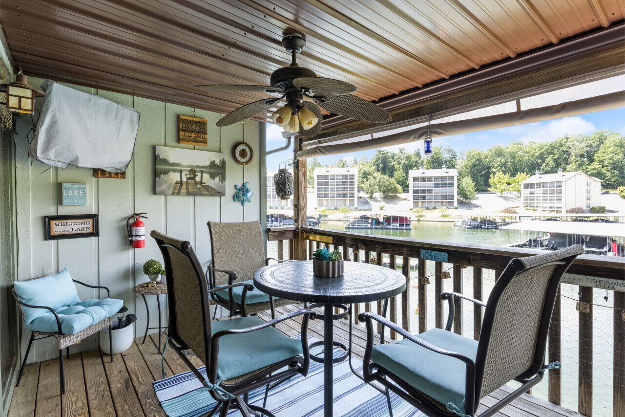 A covered deck with a table and chairs, a ceiling fan, and a view of a lake and buildings.