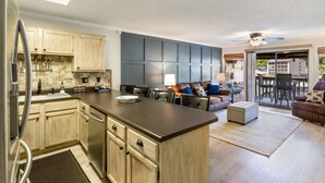 A modern kitchen with a central island, wooden cabinets, and a dining area with a couch and chairs. - Turtle Cove –  Lakefront & Indoor Pool! (Village of Four Seasons)
