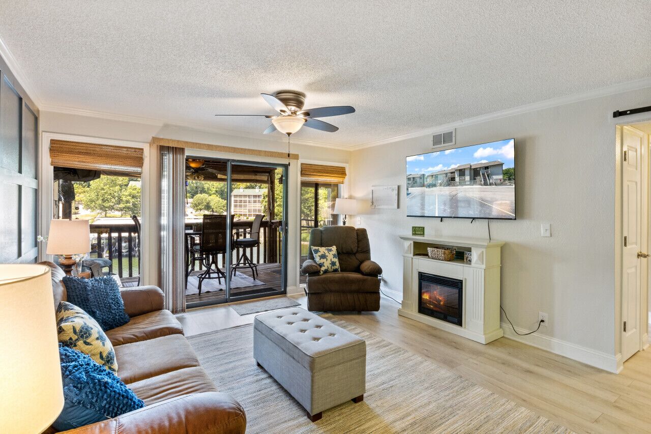 A living room with a fireplace, a ceiling fan, a television, and a sliding glass door leading to an outdoor area.
