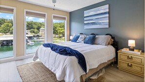 A bedroom with a bed, a nightstand, a ceiling fan, and a large window with a view of a dock and water. - Turtle Cove –  Lakefront & Indoor Pool! (Village of Four Seasons)