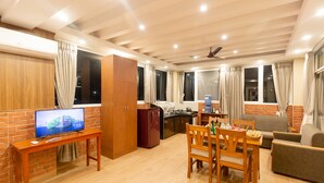 A modern living room with a wooden TV stand, a dining table with chairs, a sofa, and a kitchen area with a refrigerator and a water dispenser. - Paradise Boutique Hotel (Pokhara)