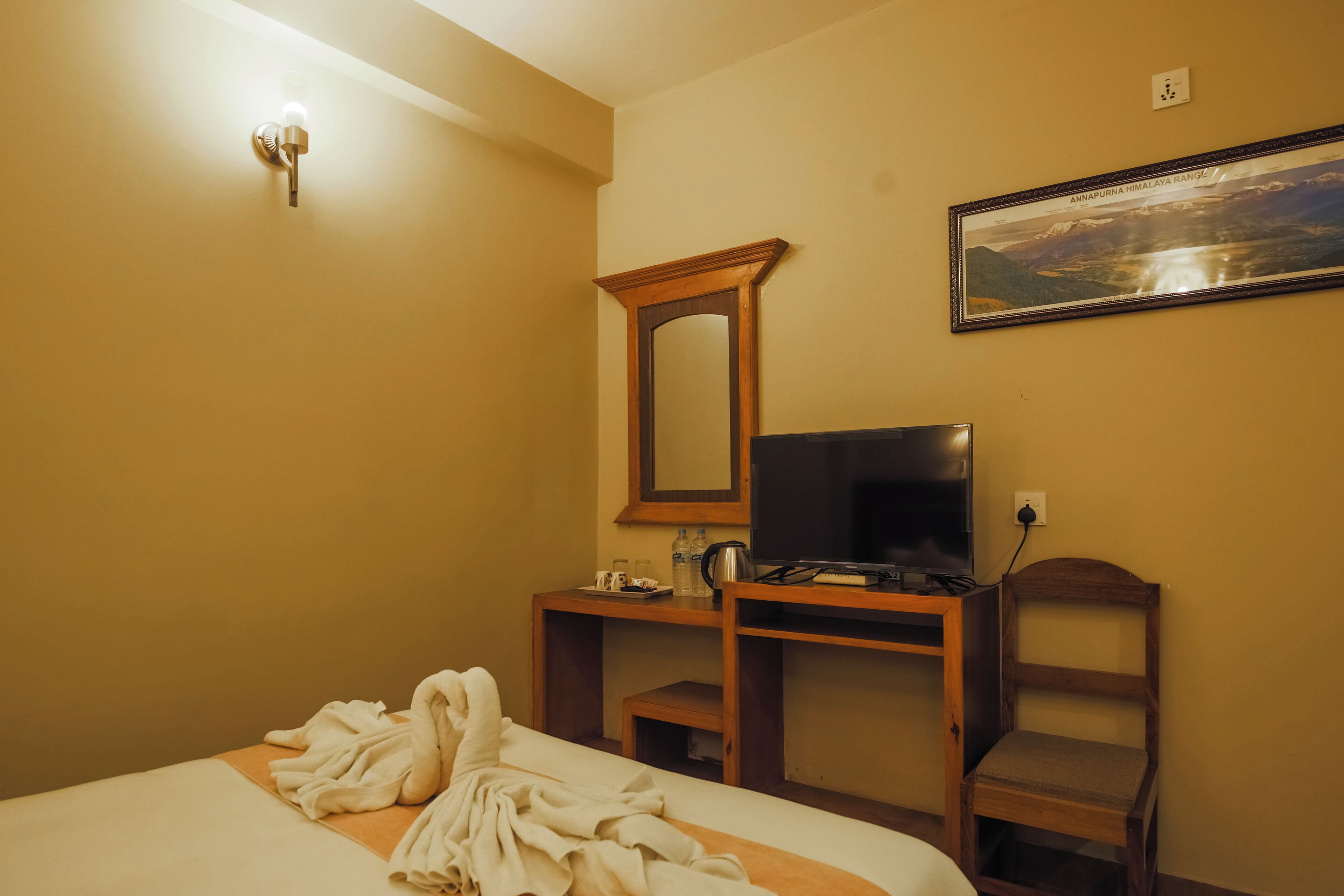 Ein Hotelzimmer mit einem Bett, einem Fernseher, einem Holztisch, einem Stuhl, einem Spiegel und einem gerahmten Bild an der Wand.