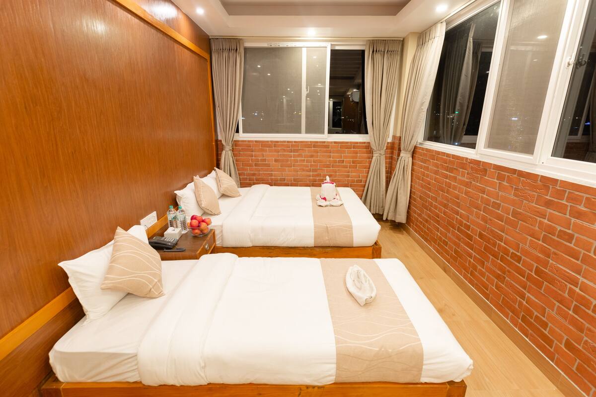 Een hotelkamer met twee bedden, een houten hoofdbord, een bakstenen muur en een raam met gordijnen.
