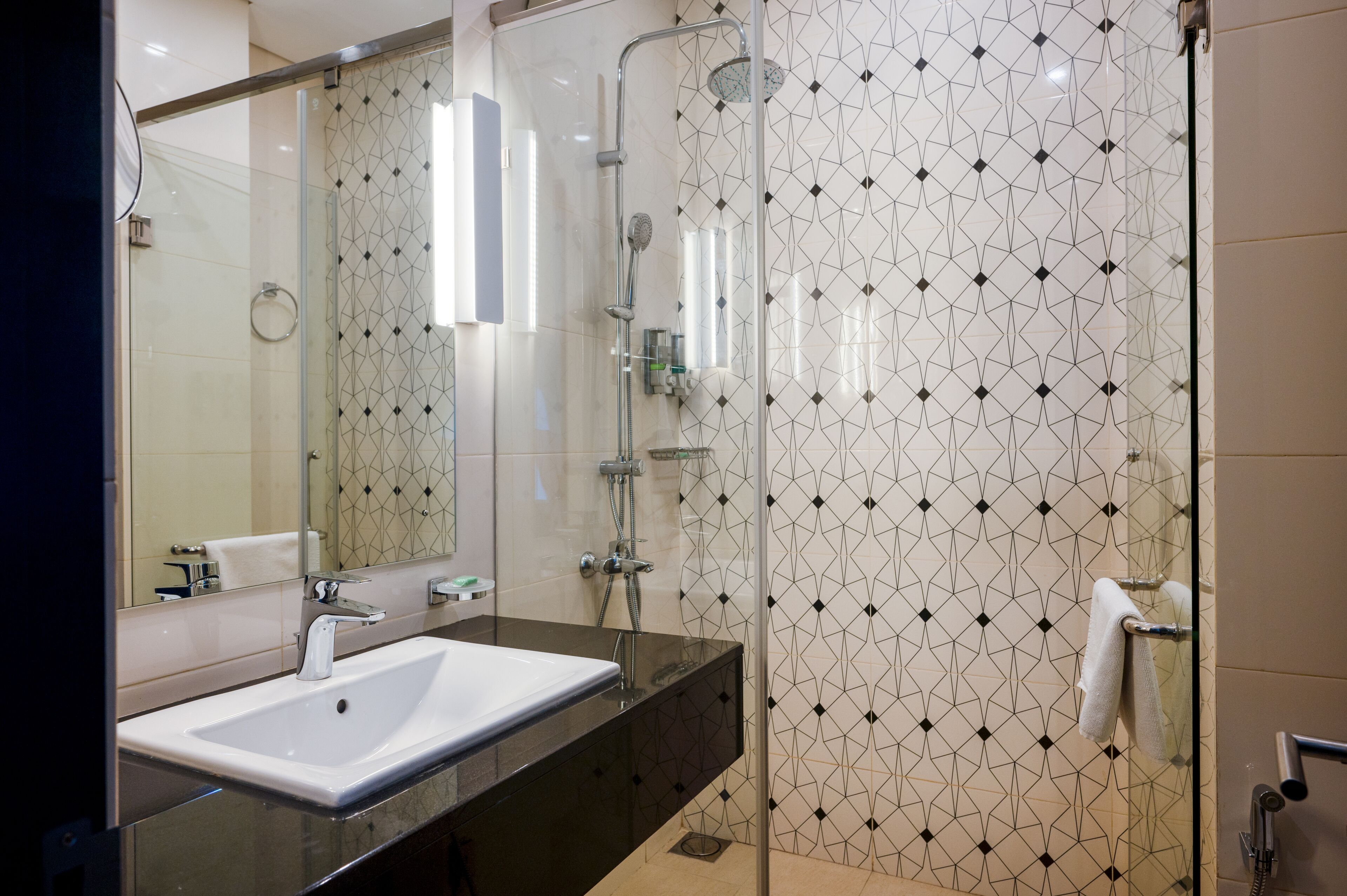 A modern bathroom with a glass-enclosed shower, a large mirror, and a black countertop.