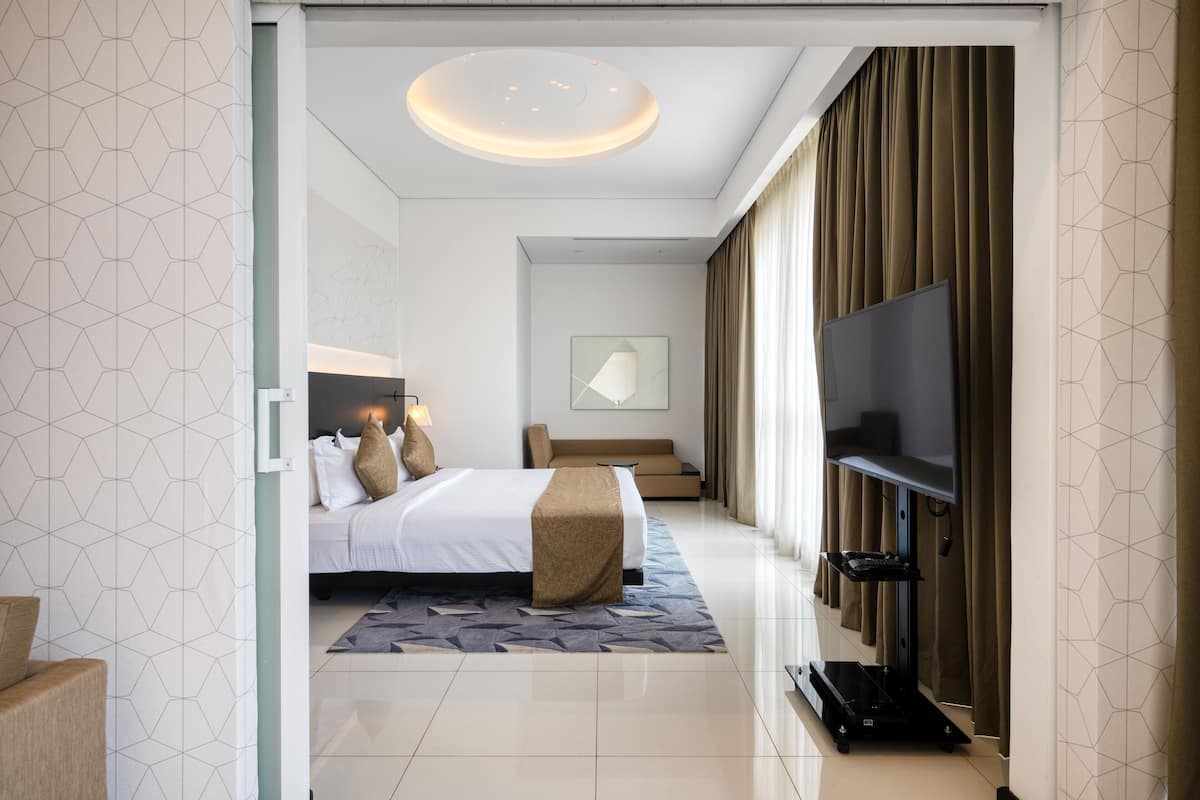 A modern hotel room with a large bed, a flat-screen TV, a sofa, and a ceiling light fixture.