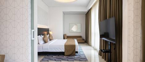 A modern hotel room with a large bed, a flat-screen TV, a sofa, and a ceiling light fixture.
