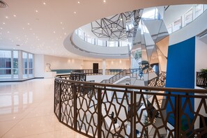 Un interior moderno con una escalera central, barandas de vidrio y un piso pulido.
