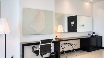 A modern hotel lobby with a reception desk, a black office chair, a standing desk, a large mirror, and a geometric artwork on the wall.