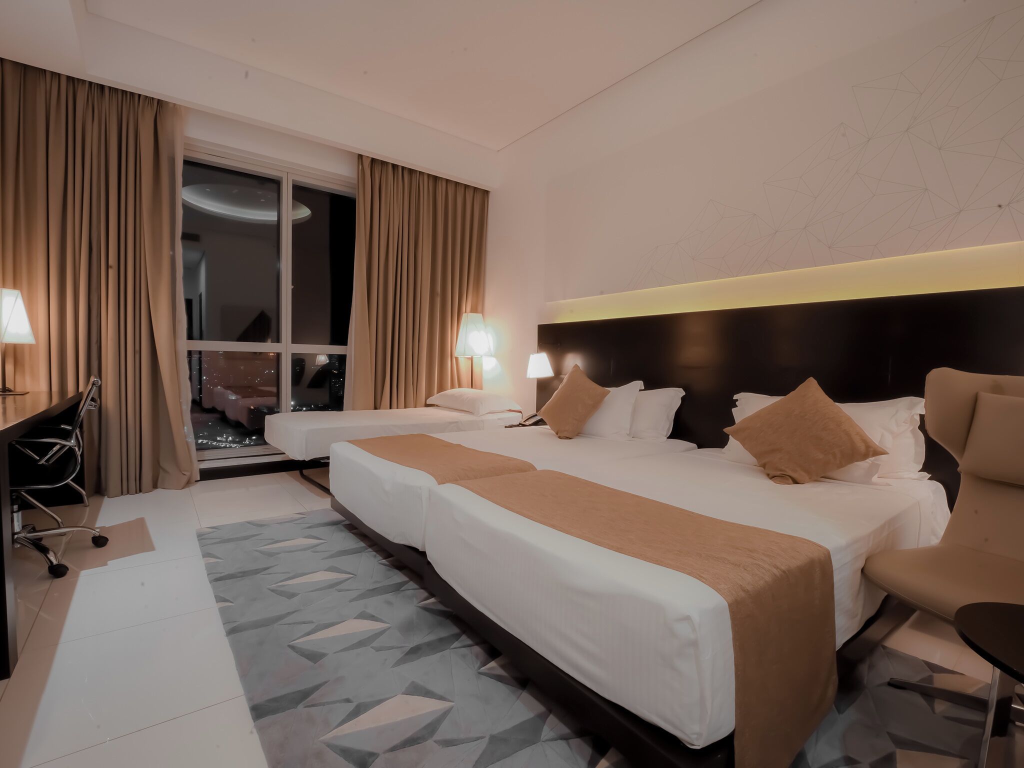 A hotel room with two beds, a desk, and a chair.
