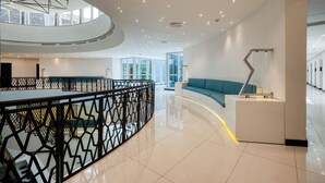 A modern interior with a curved reception desk, a blue sofa, and a geometric railing. - Orion City Hotel (Colombo)