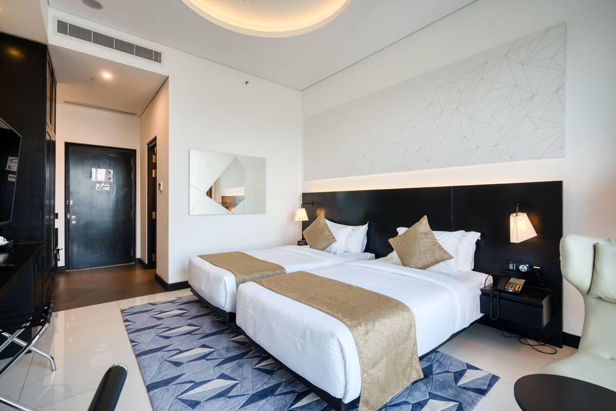 A hotel room with two beds, a desk, a chair, a desk lamp, a phone, and a wall art piece.