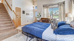 A bedroom with a large bed, a wooden staircase, and a view of the outdoors through a window. - Whistler Hollow! Family Home, Bball Court, Firepit (Colorado Springs)