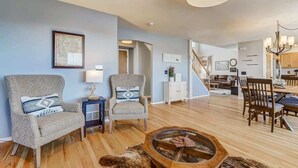 A spacious living room with a wooden floor, two armchairs, a coffee table, and a chandelier. - Whistler Hollow! Family Home, Bball Court, Firepit (Colorado Springs)