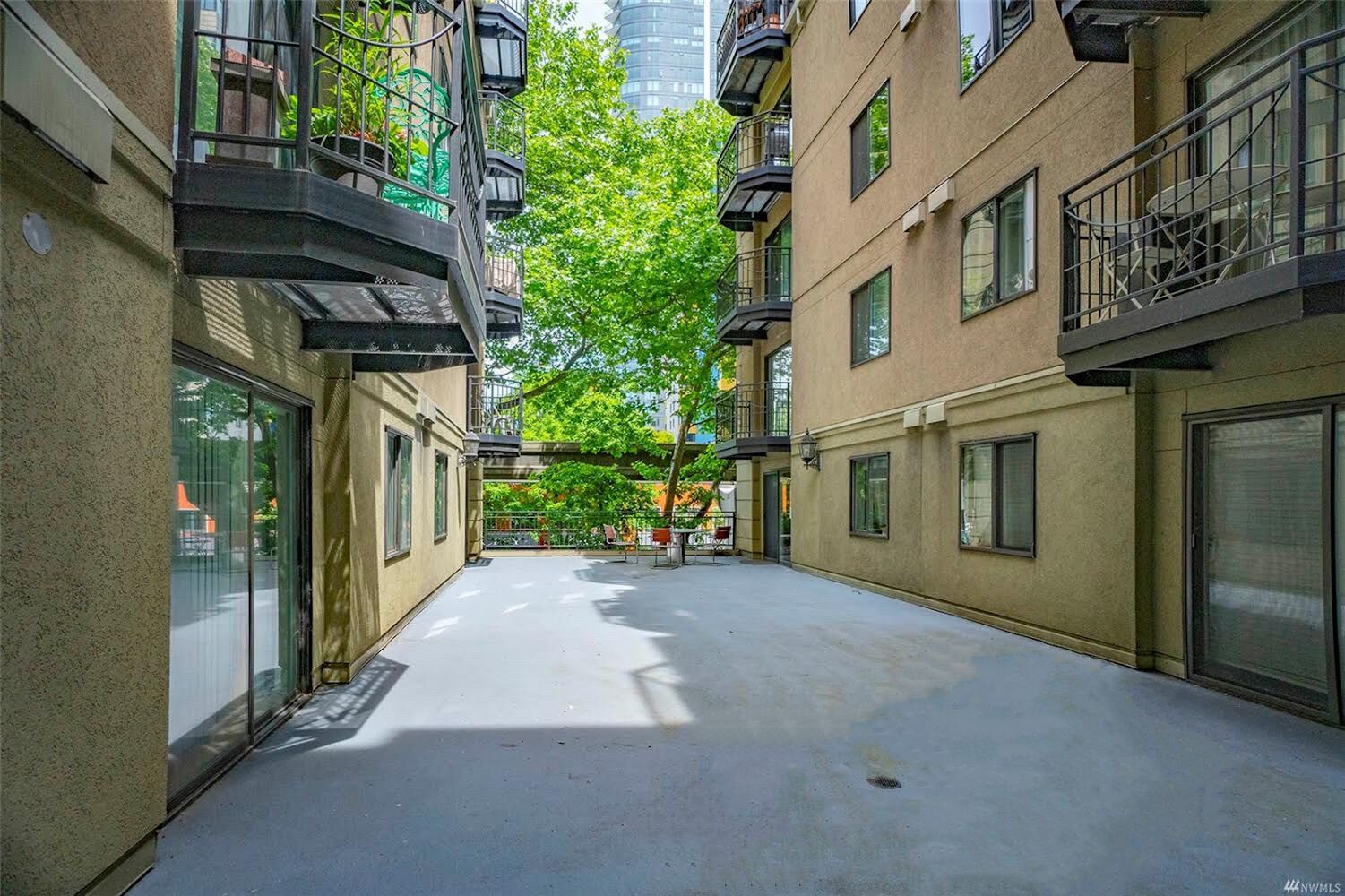 A narrow urban street with multi-story buildings, balconies, and a tree-lined pathway.