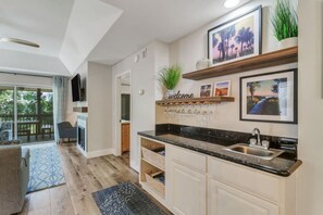 A modern kitchen with a black countertop, white cabinets, and a built-in sink. There are framed pictures on the wall and a welcome sign above the sink.