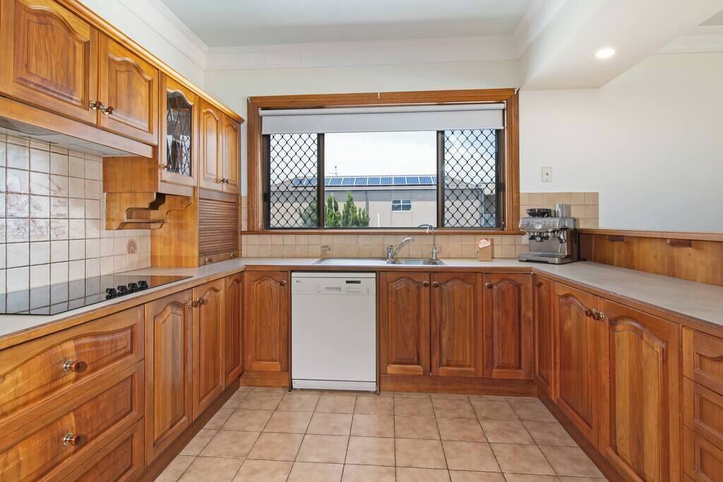 A kitchen with wooden cabinets, a dishwasher, a window with a view, and a tiled backsplash.