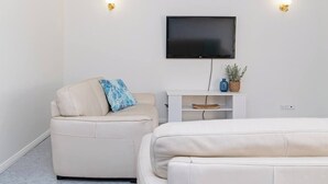 Ein modernes Zimmer mit einem wandmontierten Flachbildfernseher, einem weißen Sofa und einem kleinen Sessel mit blauem Kissen.