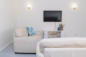 Moderni huone, jossa on seinälle asennettu taulutelevisio, valkoinen sohva ja pienempi nojatuoli, jossa on sininen koristetyyny.