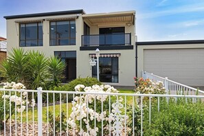 Ein modernes, zweistöckiges Haus mit Balkon, Garage und einem gepflegten Garten mit weißen Blumen.