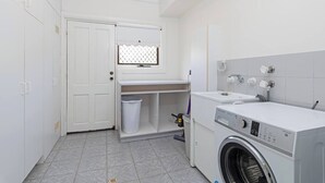 A laundry room with a washing machine, a sink, a drying rack, and a door with a window.