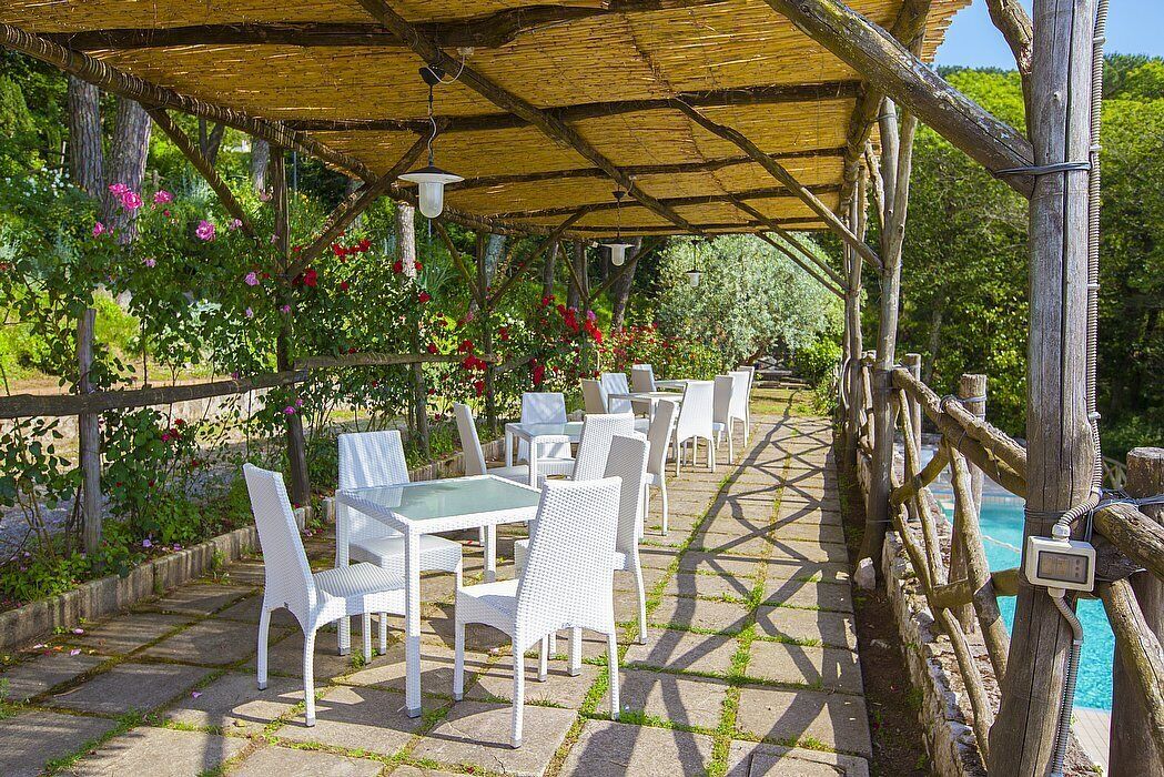 Une terrasse extérieure avec des meubles en osier blanc, un toit de chaume et une piscine.