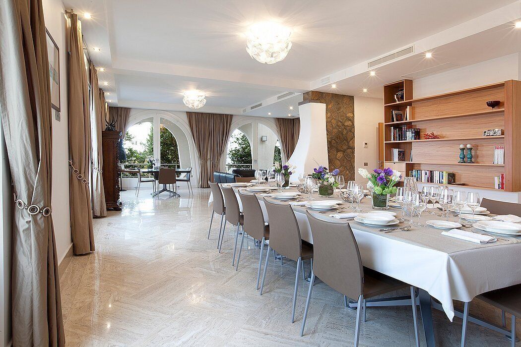 A dining area with a long table set for a meal, chairs, and a bookshelf.