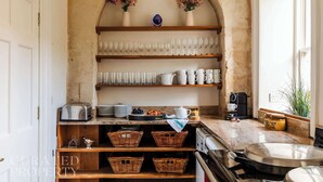 A kitchen with a stone archway, shelves with glassware, baskets, and a coffee machine. - The Admirals House - Central Bath & Free Parking! (Bath)